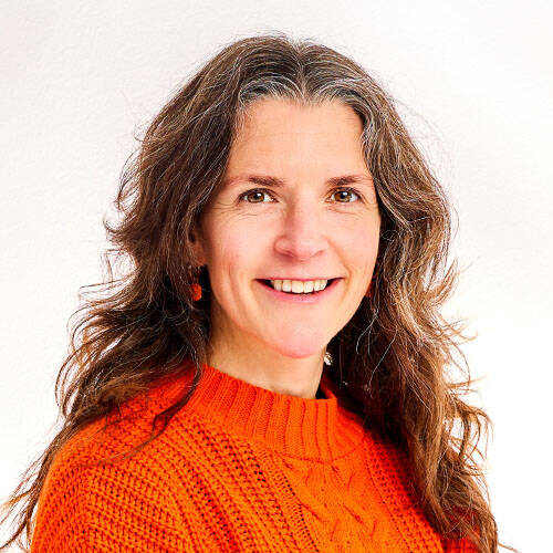 Smiling woman in orange jumper, white background.