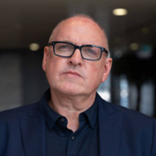 Bald man with glasses in a suit indoors.