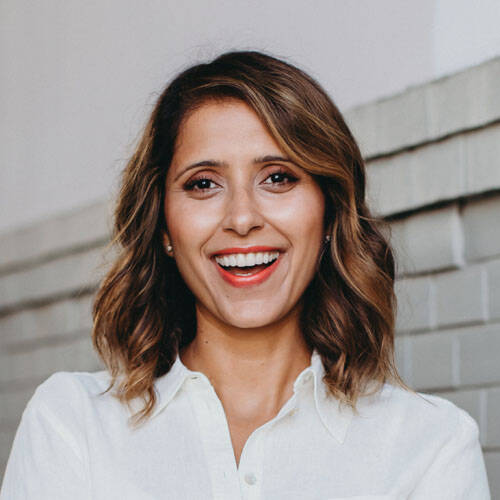Smiling woman in white shirt against brick wall.